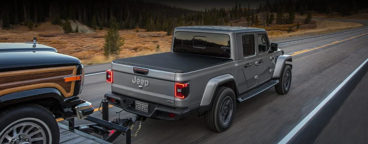Grey 2022 Jeep Gladiator towing a vehicle down a road.&nbsp;