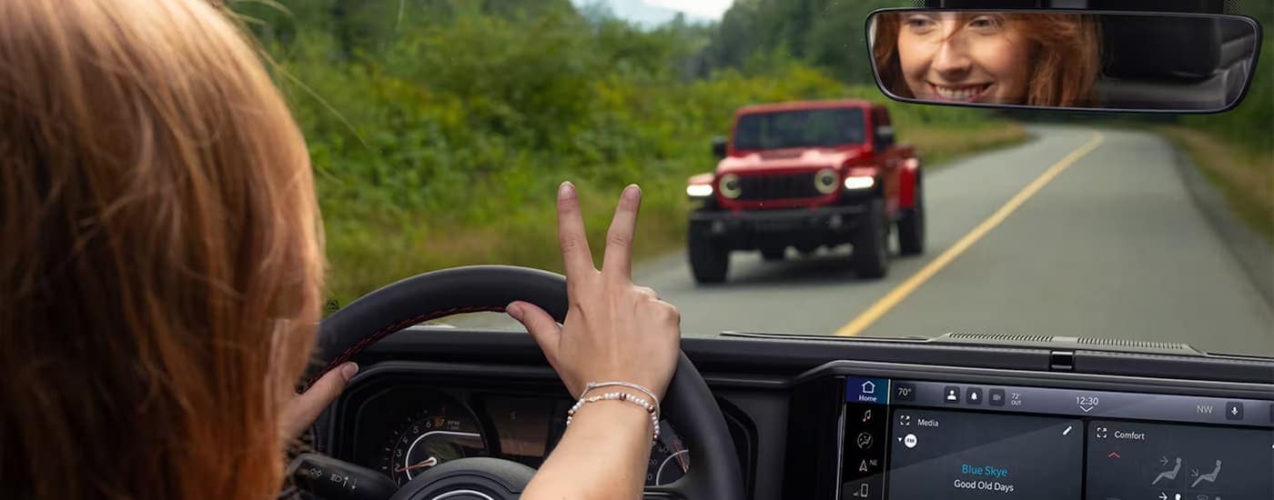 Person waving to a red 2025 Jeep Wrangler