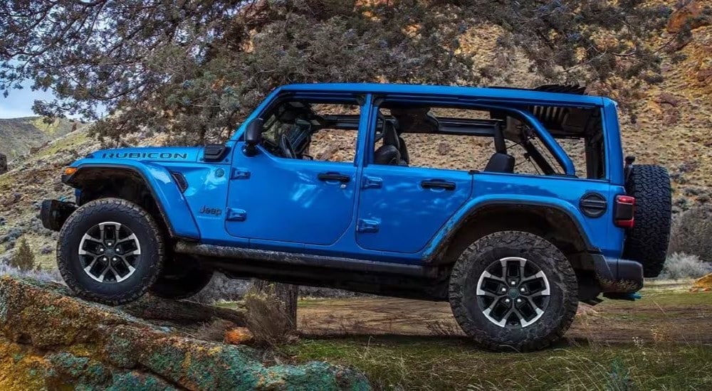 A blue 2024 Jeep Wrangler 4xe is shown from the side off-road.