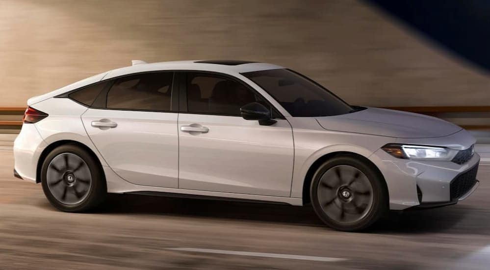 A white 2025 Honda Civic Hatchback is shown driving on a highway.